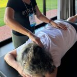Imagem mostra duas mulheres, uma aplicando reiki com imposição de mãos, enquanto a outra está deitada na maca.