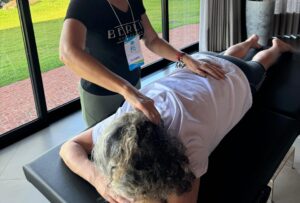 Imagem mostra duas mulheres, uma aplicando reiki com imposição de mãos, enquanto a outra está deitada na maca.