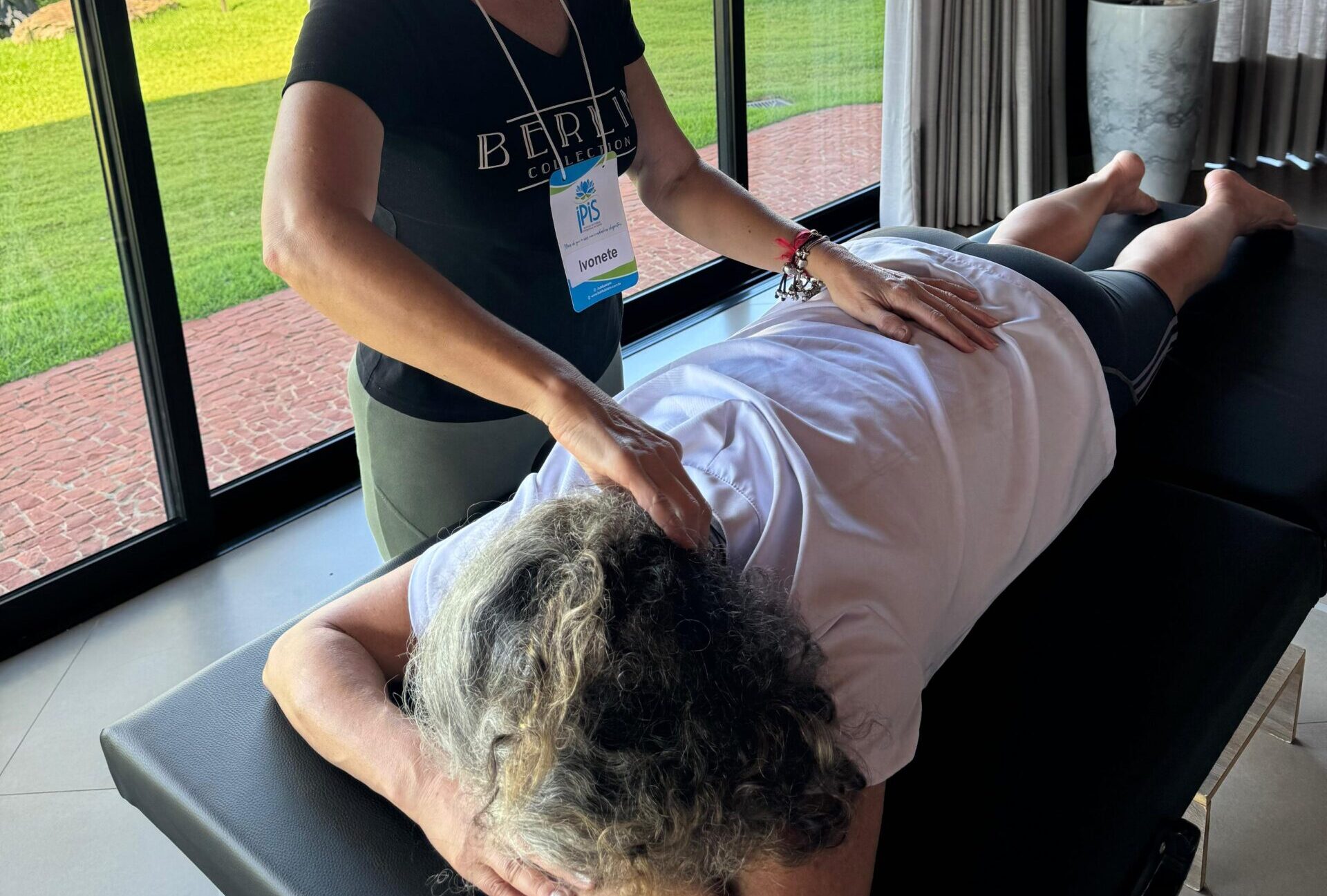 Imagem mostra duas mulheres, uma aplicando reiki com imposição de mãos, enquanto a outra está deitada na maca.